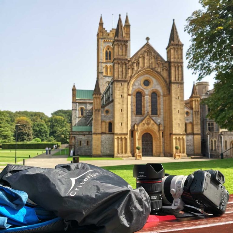 A Criterion 20L Roll Top Dry bag next to a daysack and the camera it carried to keep it clean, in-front of Buckfast Abbey in Devon.