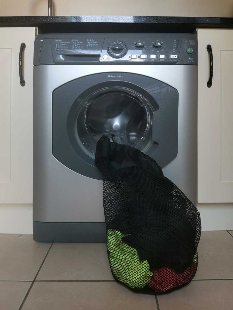 Criterion Large Mesh Storage Bag with dirty washing dirty in front of a washing machine to illustrate that the bag is not just for down sleeping bags.